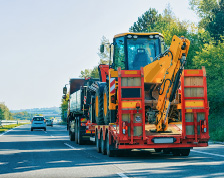 A heavy truck on a tree-lined highway pulls a trailer of large construction equipment     